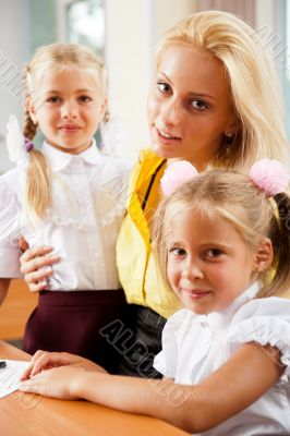 Young pretty teacher helping her little students in classroom