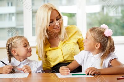 Teacher helps to little girls to make an exercises in classroom