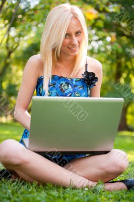 Beautiful student woman with a laptop sitting on green grass at 