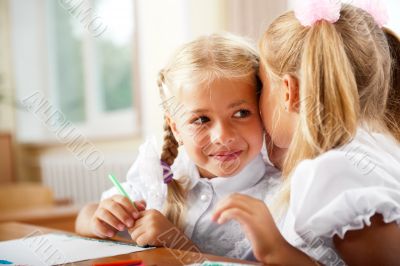 Two little girls gossip in classroom