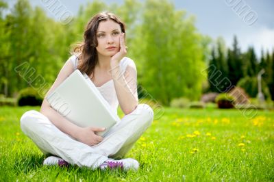 Young woman with laptop sitting on green grass