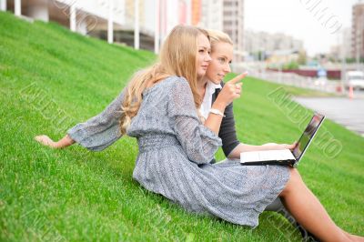 Portrait of two smiling women using laptop on a green meadow at 