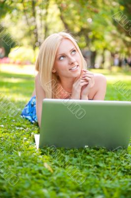 Portrait of young pretty woman resting on green grass at summe