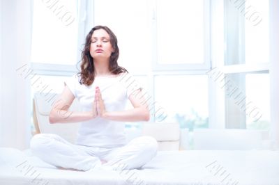 Young woman meditating with closed eyes in bright bedroom sittin