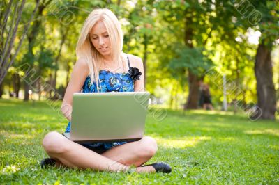 Beautiful student woman with a laptop sitting on green grass at 