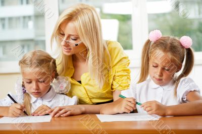 Teacher helps to little girls to make an exercises in classroom