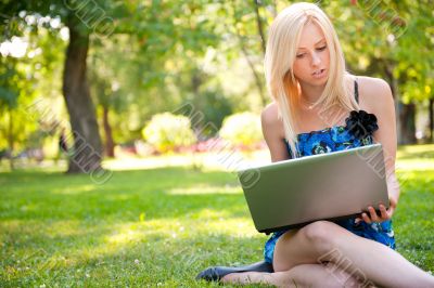 Beautiful student woman with a laptop sitting on green grass at 