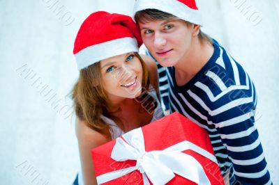 Portrait of young pretty couple standing indoors wearing Santa C