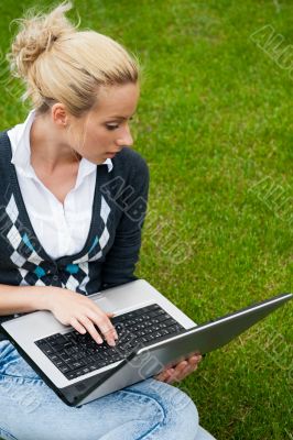Young woman with laptop sitting on green grass and looking to th