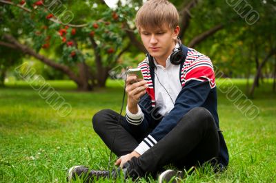 Student outside sitting on green grass and listening music via h