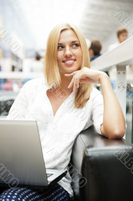 Portrait of happy blond woman using laptop at shopping mall cafe