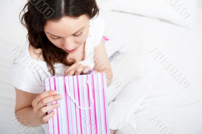 Portrait of young beautiful awake woman with gifts on bed at bed
