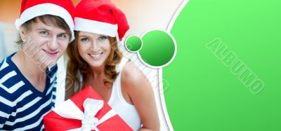 Young happy couple in Christmas hats standing together and holdi