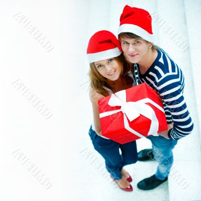 Young happy couple in Christmas hats standing together and holdi