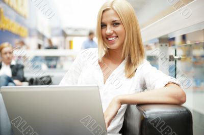 Portrait of happy blond woman using laptop at shopping mall cafe