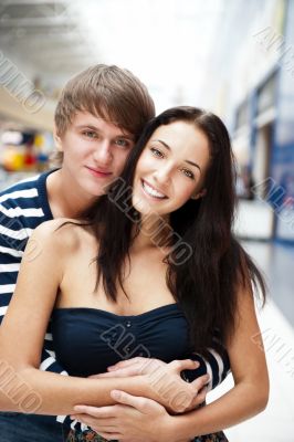Portrait of young couple embracing at shopping mall and looking 
