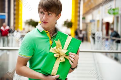 Portrait of young man inside shopping mall with gift box sitting