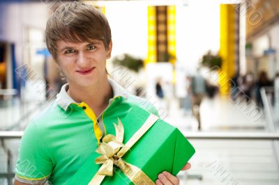 Portrait of young man inside shopping mall with gift box sitting