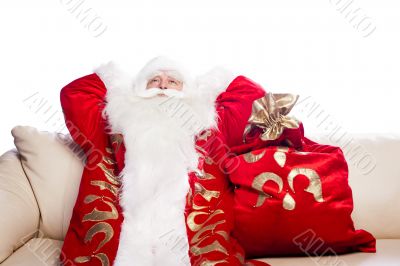 Traditional Santa Claus resting on sofa indoors and daydreaming.