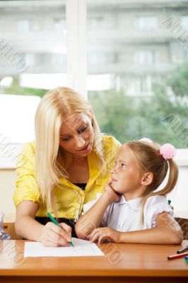 Teacher helps to little girls to make an exercises in classroom