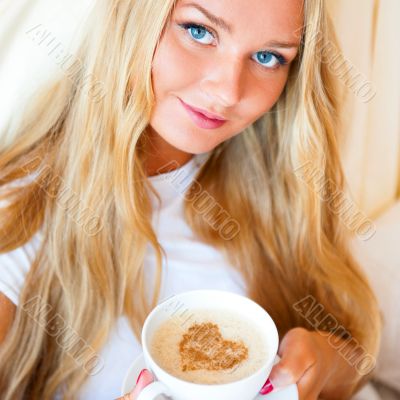 Smiling woman drinking a coffee lying on a bed at home or hotel.