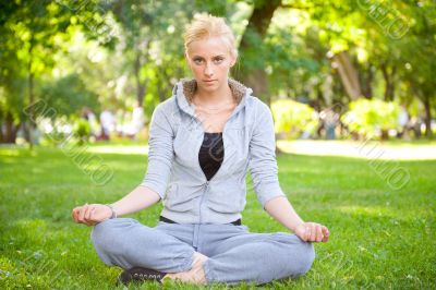 Portrait of young woman meditating in pose of lotus on green gra