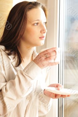 Portrait of cosy young girl standing near a window at home