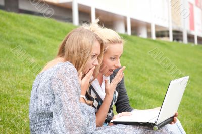 Portrait of two smiling women using laptop on a green meadow at 
