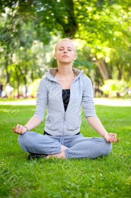 Portrait of young woman meditating in pose of lotus on green gra