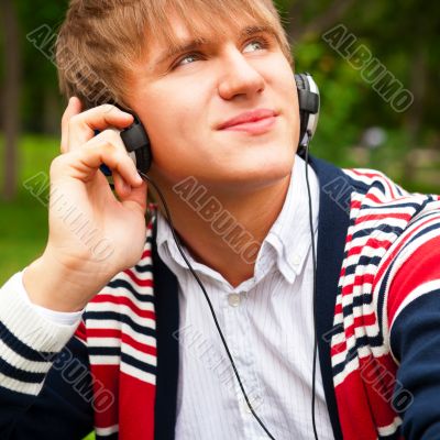 Student outside sitting on green grass and listening music via h