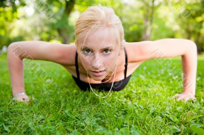 Full length of young woman doing pushups on green grass at summe