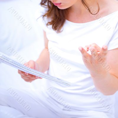 Young woman with a notebook studying at home sitting on bed. She