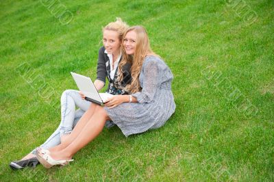 Portrait of two smiling women using laptop on a green meadow at 