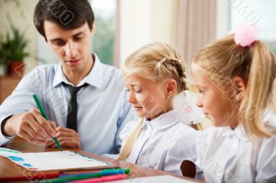 Teacher helping students with schoolwork in school classroom. Ho