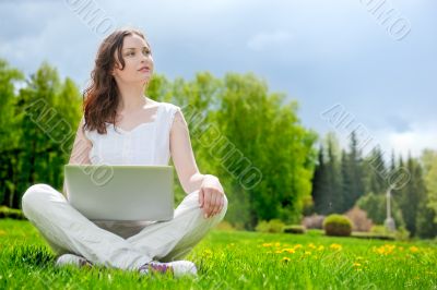 Young woman with laptop sitting on green grass