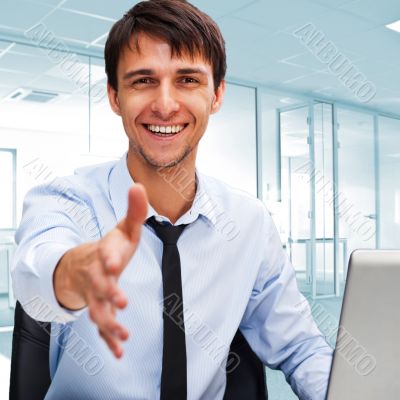 Businessman gives a handshake. Sitting near his laptop at his de