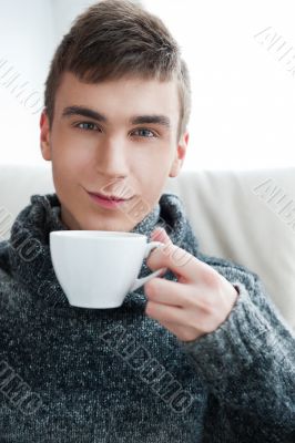 Portrait of a young man drinking coffee while sitting on armchai