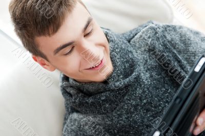Happy young handsome man at home, smiling and using his tablet c