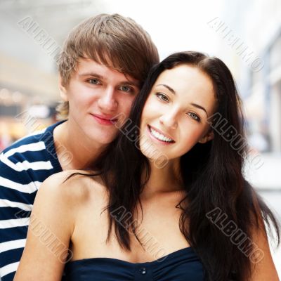 Portrait of young couple embracing at shopping mall and looking 