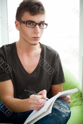Young adult man writing in his copybook while sitting on a large