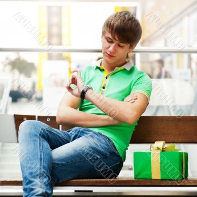 Portrait of young man inside shopping mall with gift box sitting