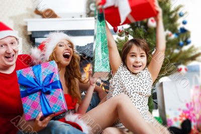 Young happy family near a Christmas tree at home holding gift an