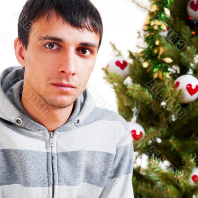 Young calm man sitting in front of Christmas tree