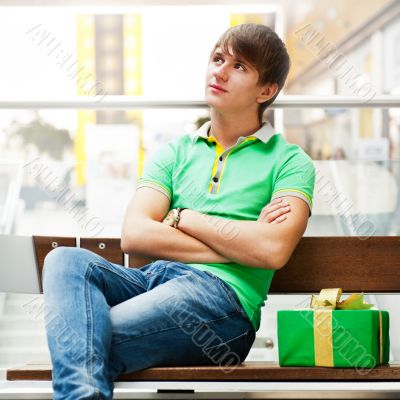 Portrait of young man inside shopping mall with gift box sitting