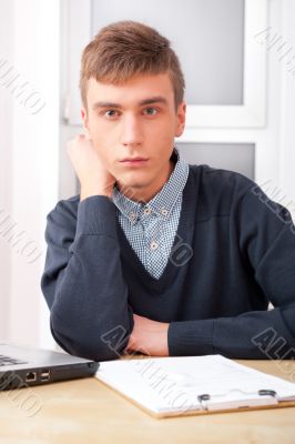 Young student man working in bright room, sitting at desk, using