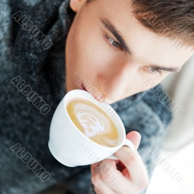 Portrait of a young man drinking coffee while sitting on armchai