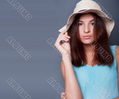 Confident woman with arms near her head holding hat against a bl