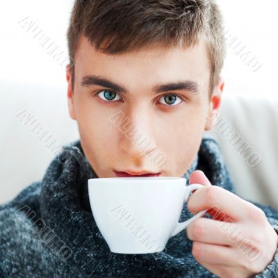 Portrait of a young man drinking coffee while sitting on armchai