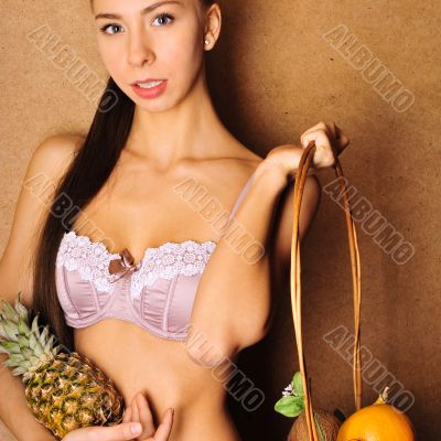 Portrait of young sexy woman holding fruit in her arms, standing