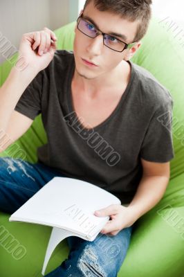 Young adult man writing in his copybook while sitting on a large